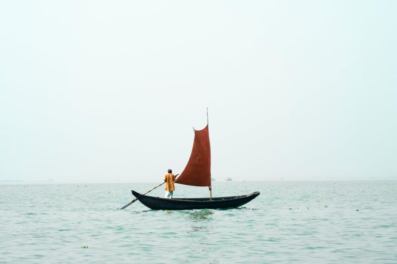 a man rowing a small boat with a sail
