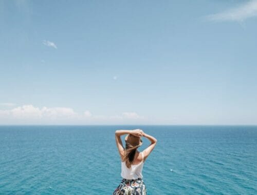 a woman with a hat looking at the blue sea under blue sky