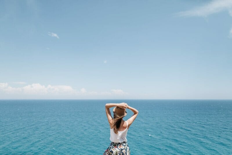 a woman with a hat looking at the blue sea under blue sky